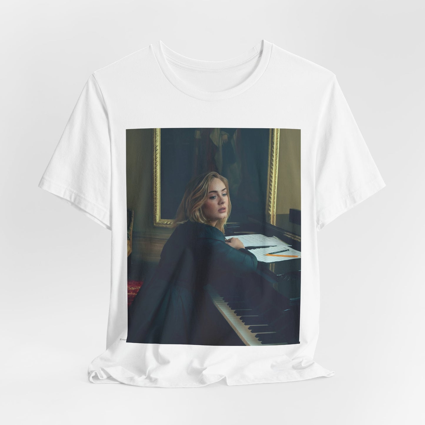 A black graphic t-shirt featuring a black and white photo of Adele sitting at a piano, with a focused and emotional expression as if performing.