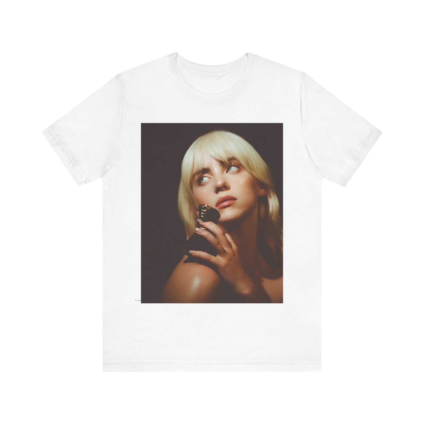 A soft, close-up portrait of Billie Eilish with dark hair looking down thoughtfully, printed on a graphic t-shirt.