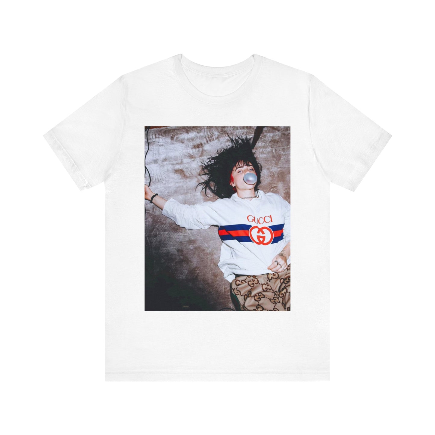 An overhead, pop-art style photo of Billie Eilish lying on the floor wearing a Gucci sweatshirt and blowing a bubblegum bubble, printed on a graphic t-shirt.