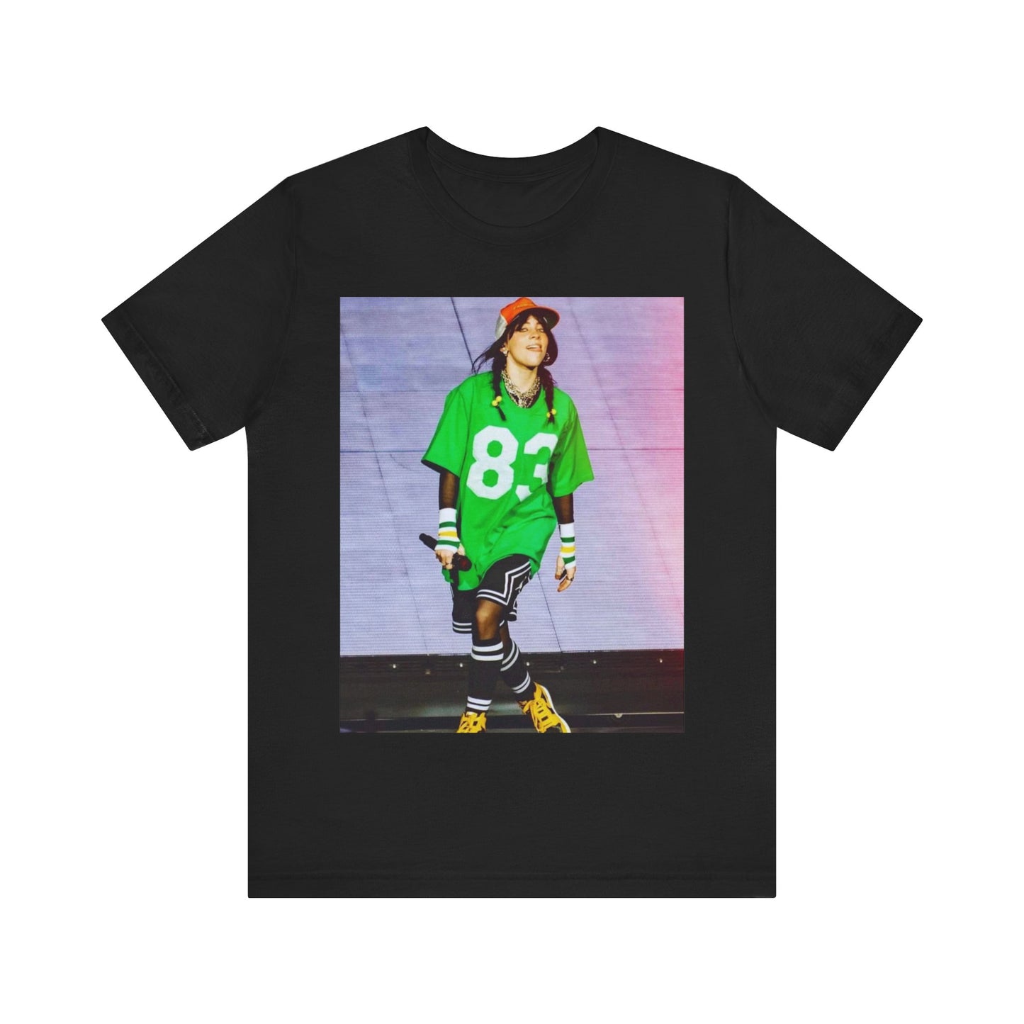 Billie Eilish performing on stage wearing a large green basketball jersey with the number 83 and an orange backwards cap.