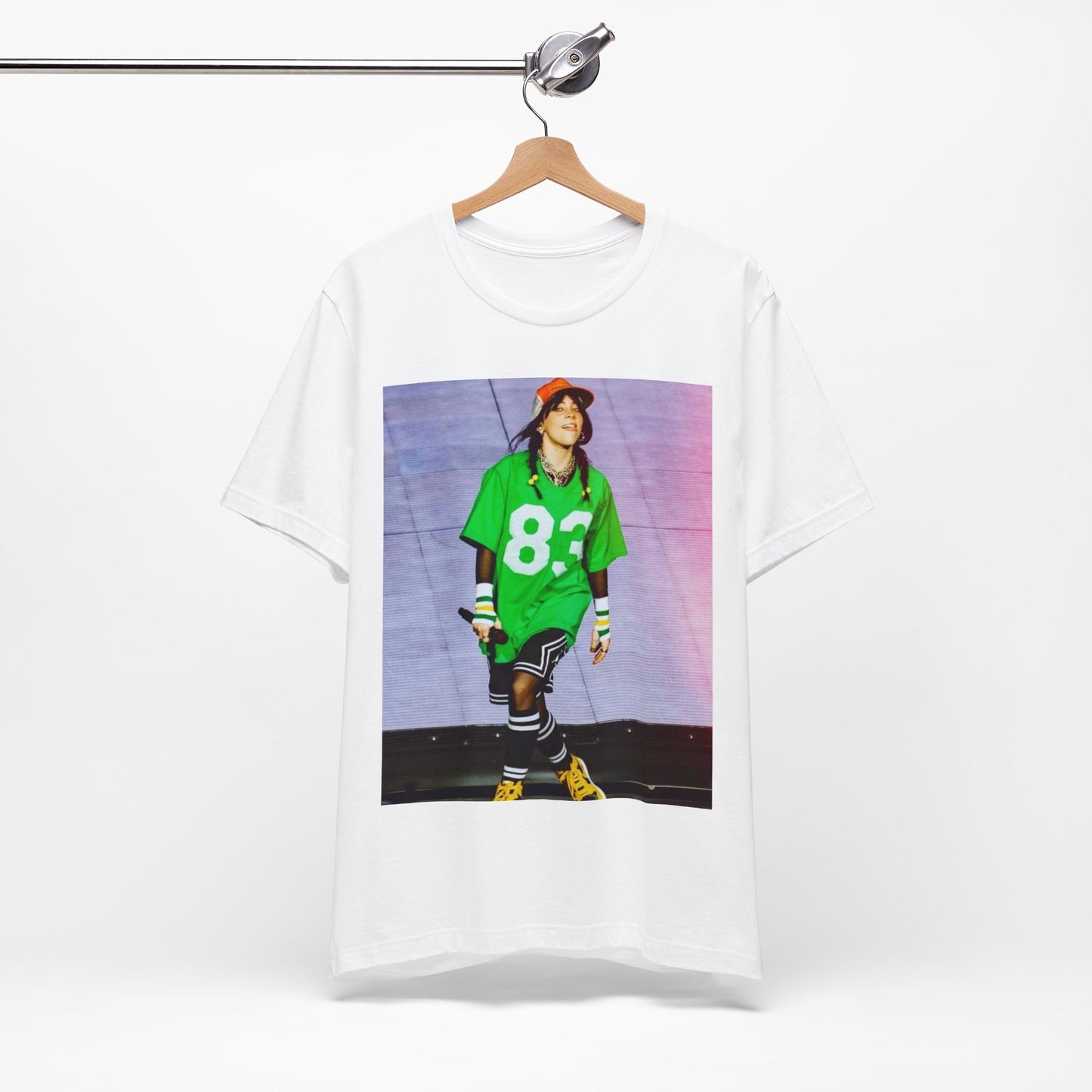 Billie Eilish performing on stage wearing a large green basketball jersey with the number 83 and an orange backwards cap.