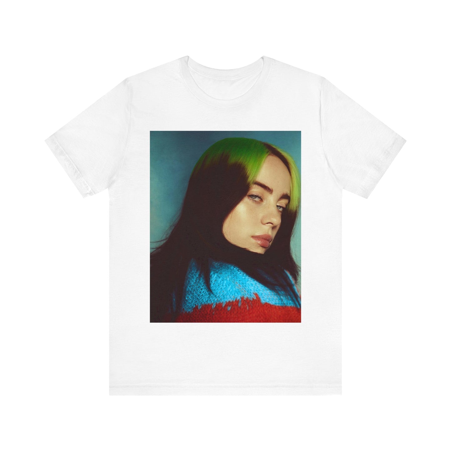 A close-up portrait of Billie Eilish with her signature green-root and black hair, wearing a blue and red sweater, printed on a graphic t-shirt.