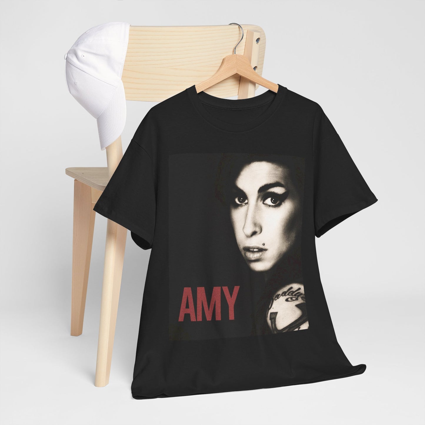 A black graphic t-shirt featuring a stylized graphic of Amy Winehouse, designed to represent her enduring legacy, possibly with her name or iconic elements.