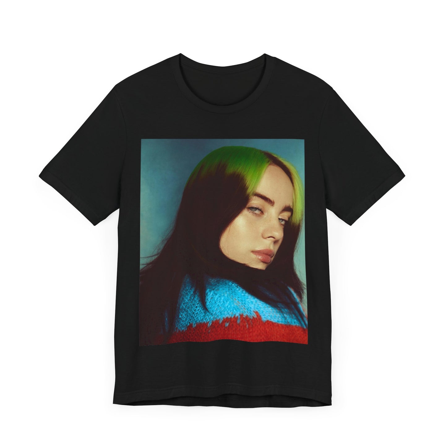 A close-up portrait of Billie Eilish with her signature green-root and black hair, wearing a blue and red sweater, printed on a graphic t-shirt.