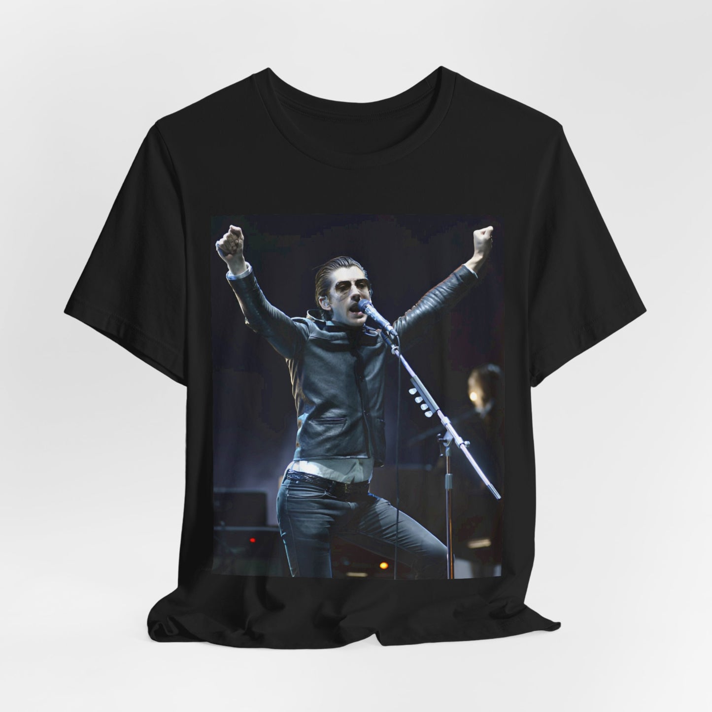A black graphic t-shirt featuring a graphic or photo of Arctic Monkeys performing live on stage, with a Britpop aesthetic.