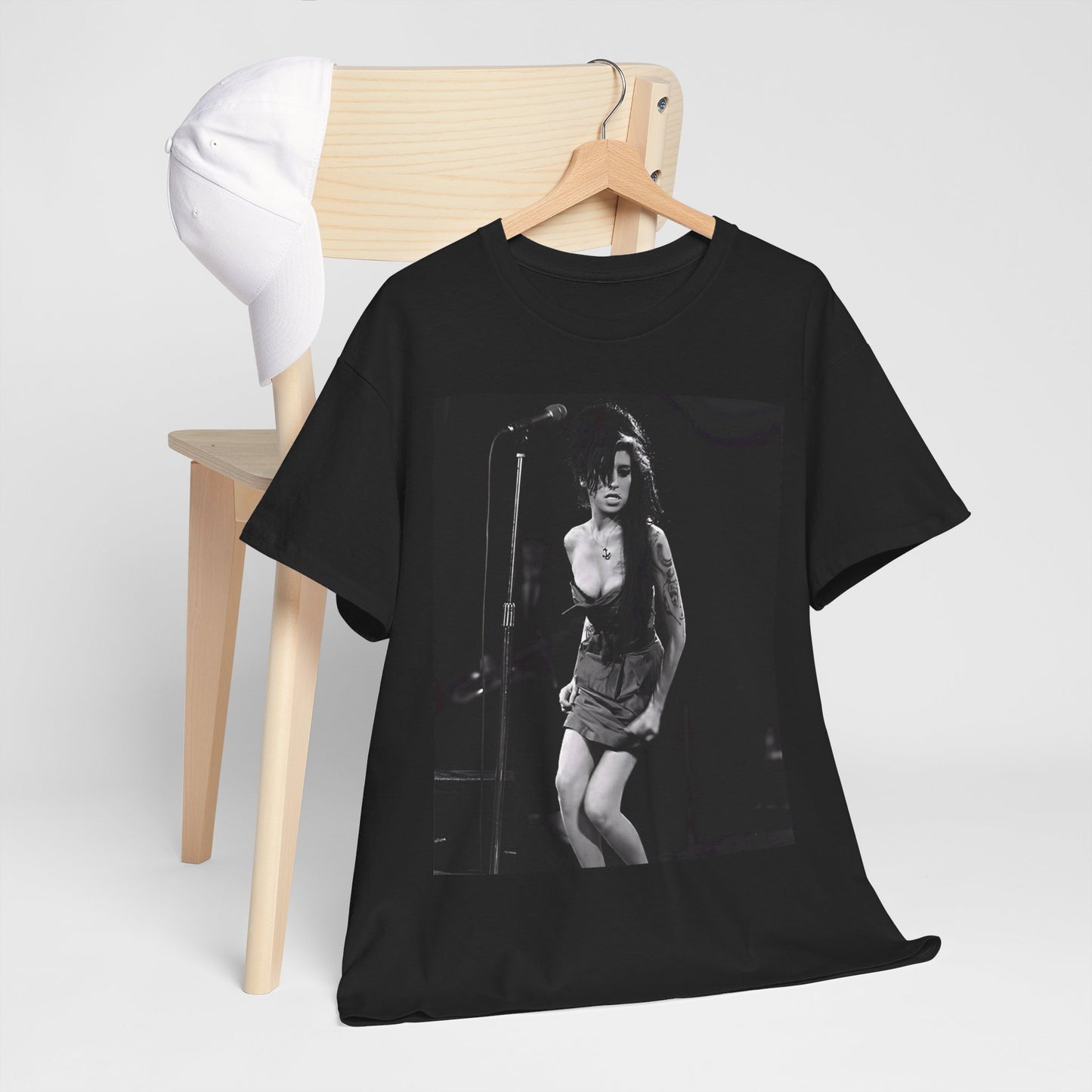 A black graphic t-shirt featuring a photo of Amy Winehouse performing live on stage at nightfall, with stage lighting effects.