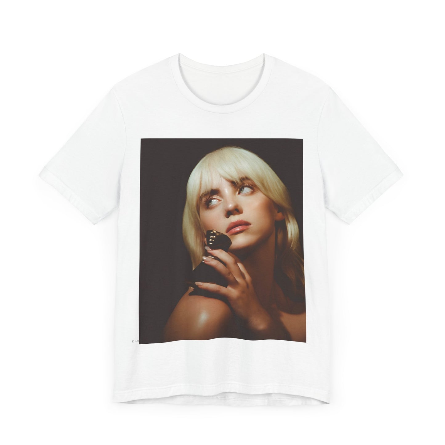 A soft, close-up portrait of Billie Eilish with dark hair looking down thoughtfully, printed on a graphic t-shirt.