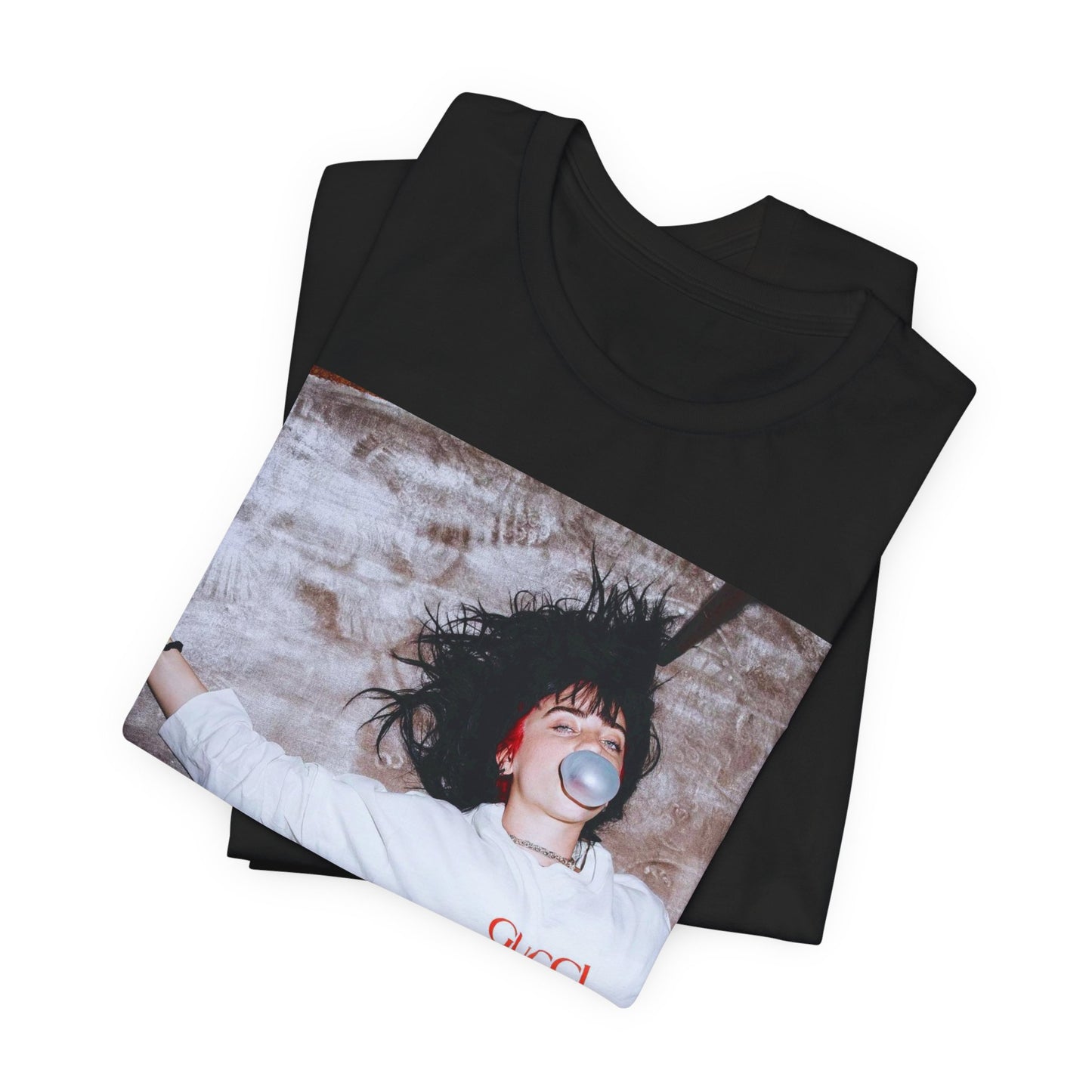 An overhead, pop-art style photo of Billie Eilish lying on the floor wearing a Gucci sweatshirt and blowing a bubblegum bubble, printed on a graphic t-shirt.