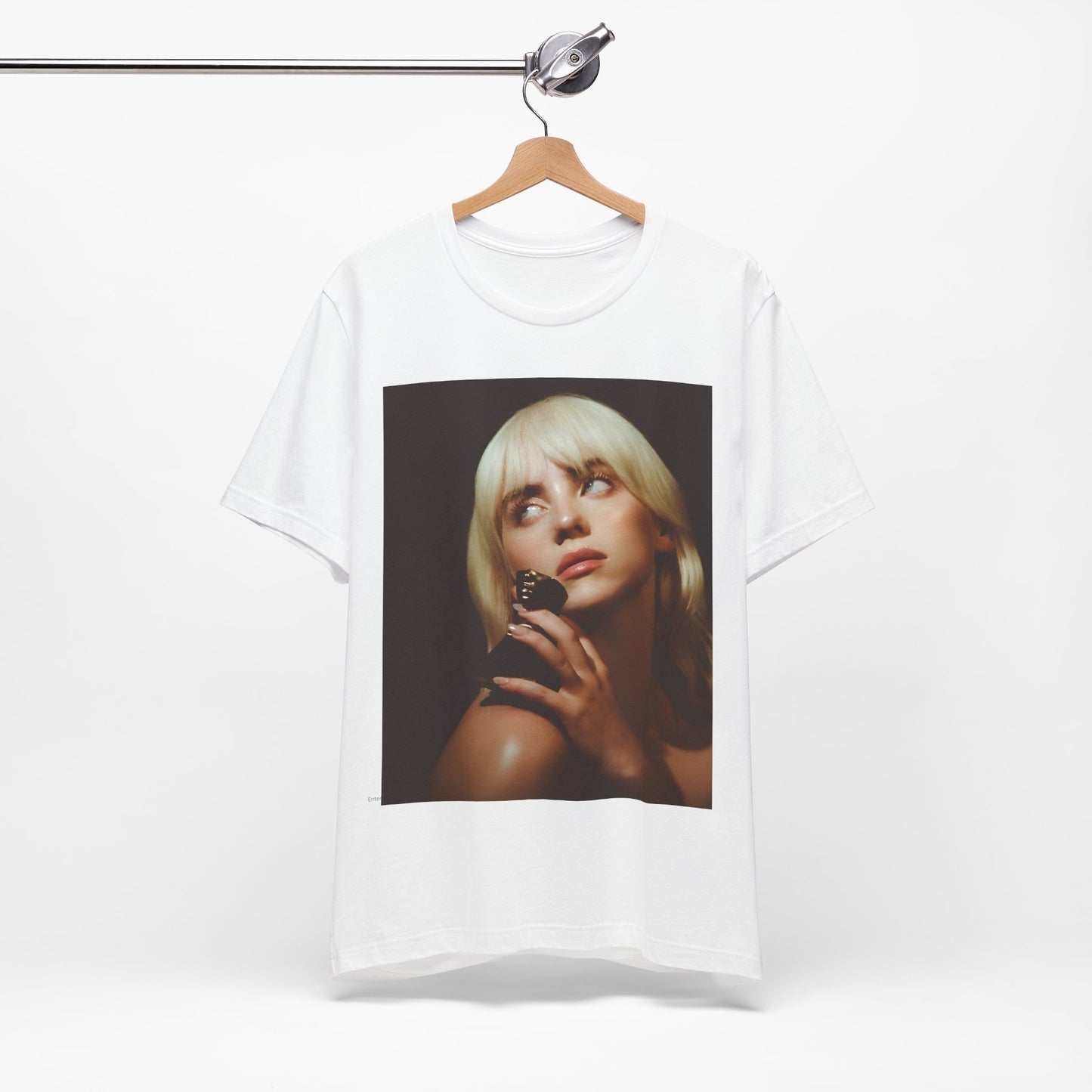 A soft, close-up portrait of Billie Eilish with dark hair looking down thoughtfully, printed on a graphic t-shirt.