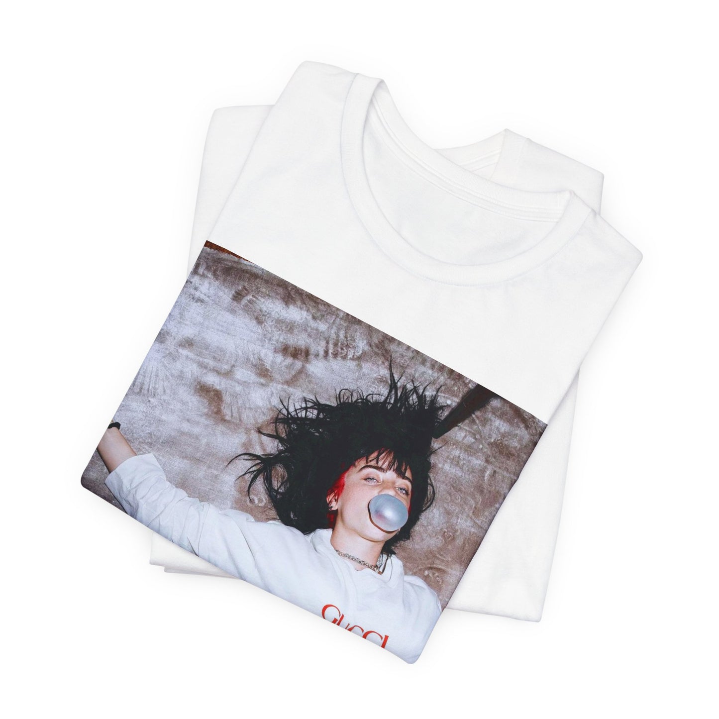 An overhead, pop-art style photo of Billie Eilish lying on the floor wearing a Gucci sweatshirt and blowing a bubblegum bubble, printed on a graphic t-shirt.