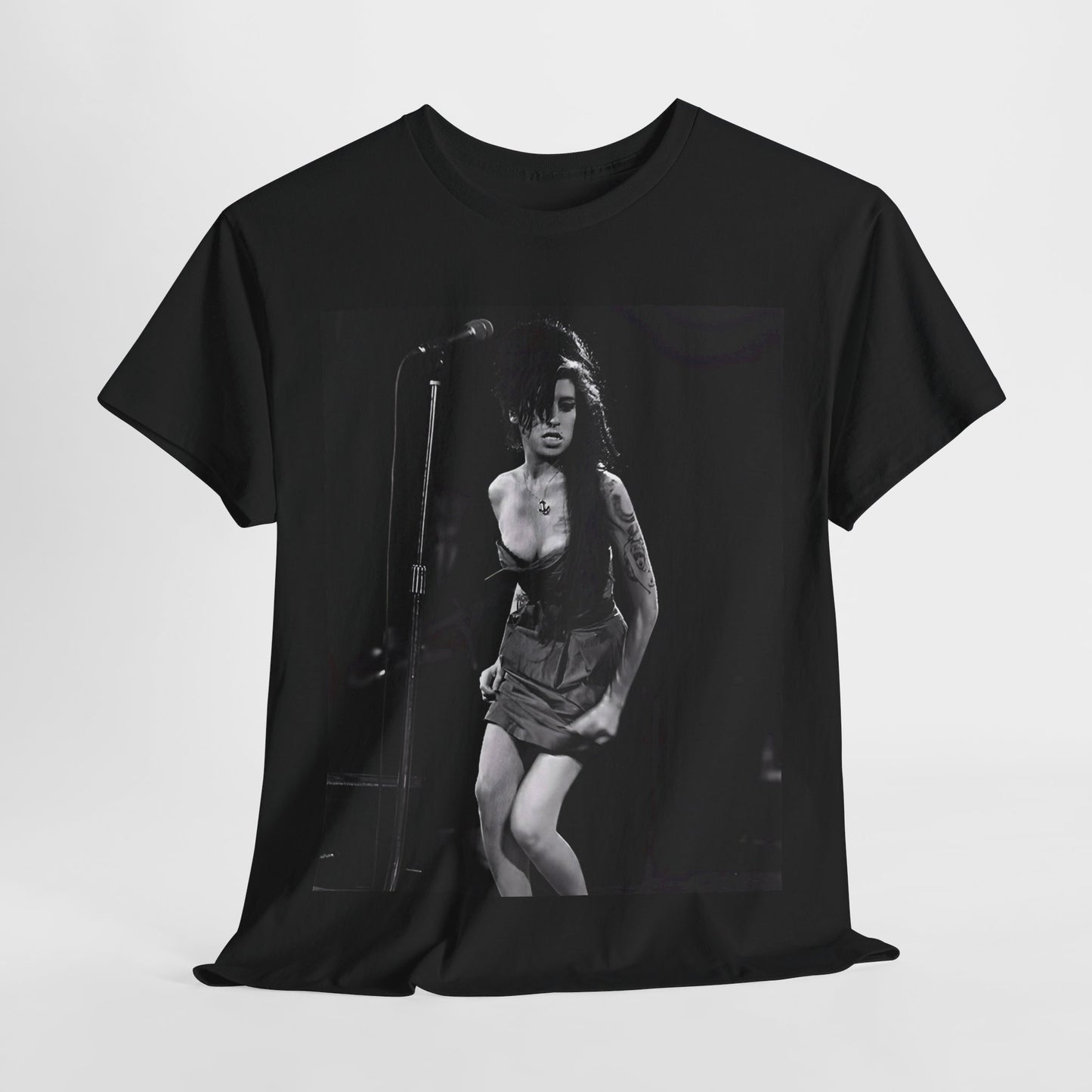 A black graphic t-shirt featuring a photo of Amy Winehouse performing live on stage at nightfall, with stage lighting effects.