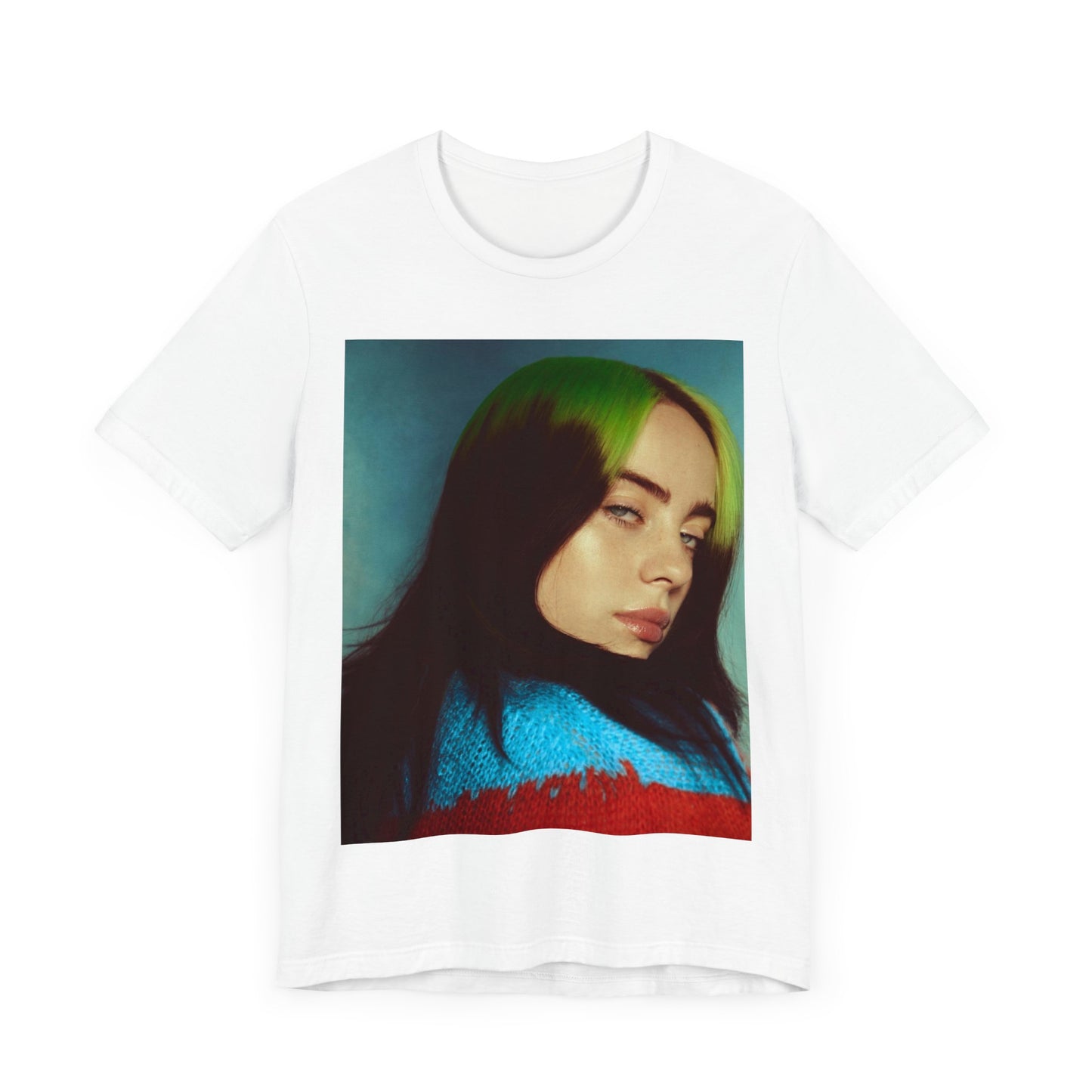 A close-up portrait of Billie Eilish with her signature green-root and black hair, wearing a blue and red sweater, printed on a graphic t-shirt.