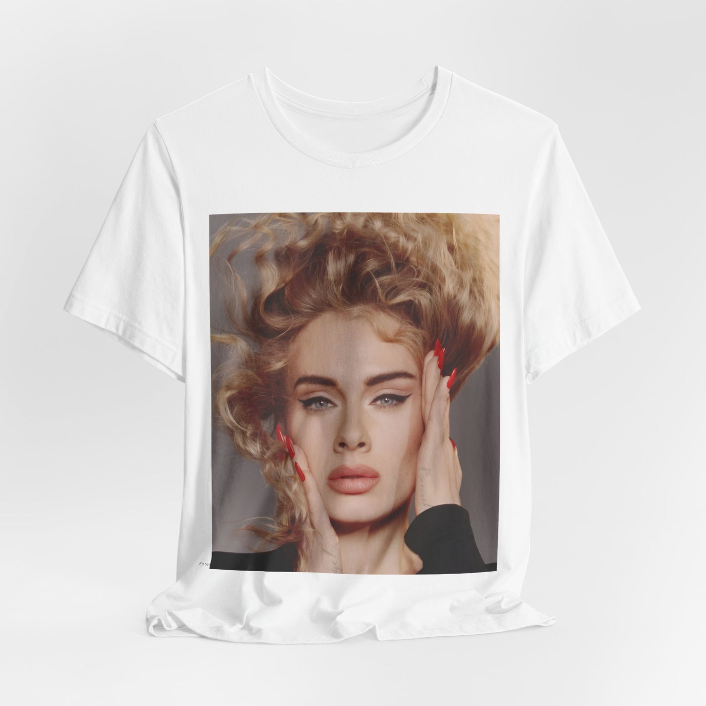 A black graphic t-shirt featuring a detailed, artistic black and white portrait of Adele with her hair dramatically caught in a breeze around her face and her hands gently placed on her cheeks.