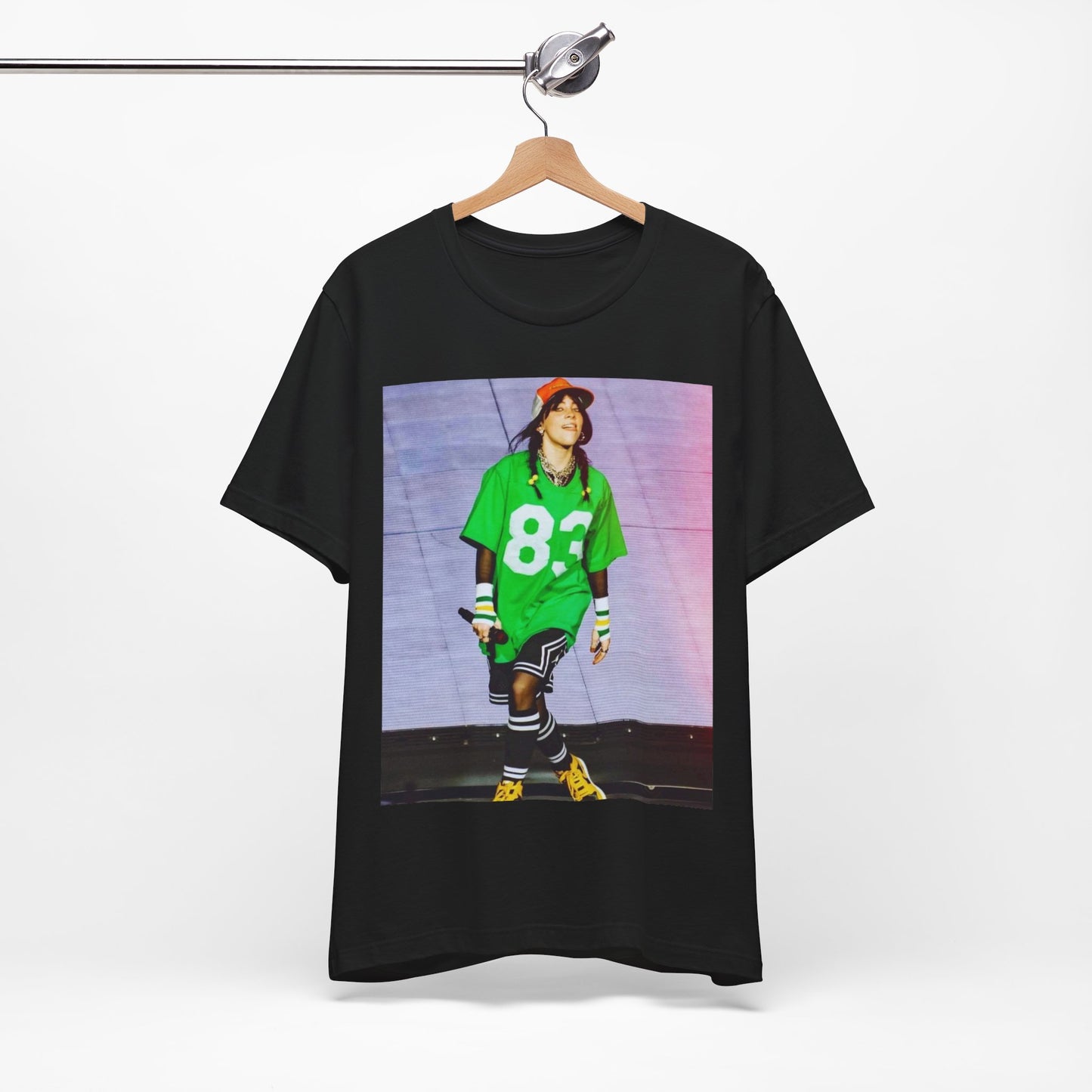 Billie Eilish performing on stage wearing a large green basketball jersey with the number 83 and an orange backwards cap.