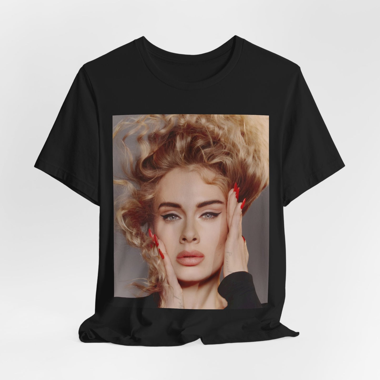 A black graphic t-shirt featuring a detailed, artistic black and white portrait of Adele with her hair dramatically caught in a breeze around her face and her hands gently placed on her cheeks.