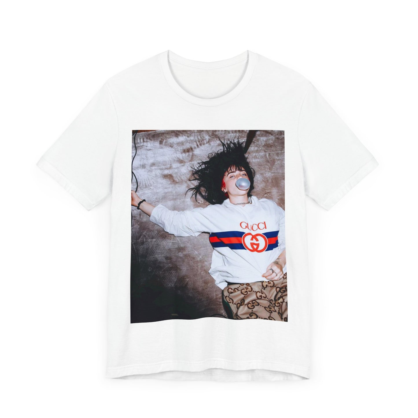 An overhead, pop-art style photo of Billie Eilish lying on the floor wearing a Gucci sweatshirt and blowing a bubblegum bubble, printed on a graphic t-shirt.