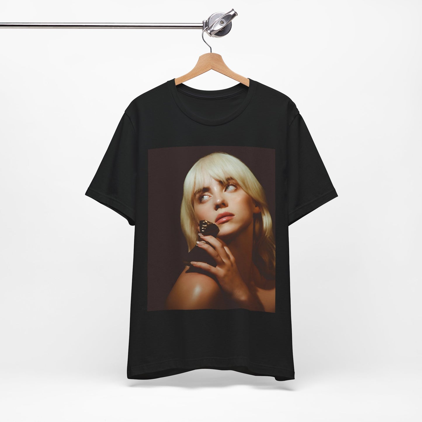A soft, close-up portrait of Billie Eilish with dark hair looking down thoughtfully, printed on a graphic t-shirt.