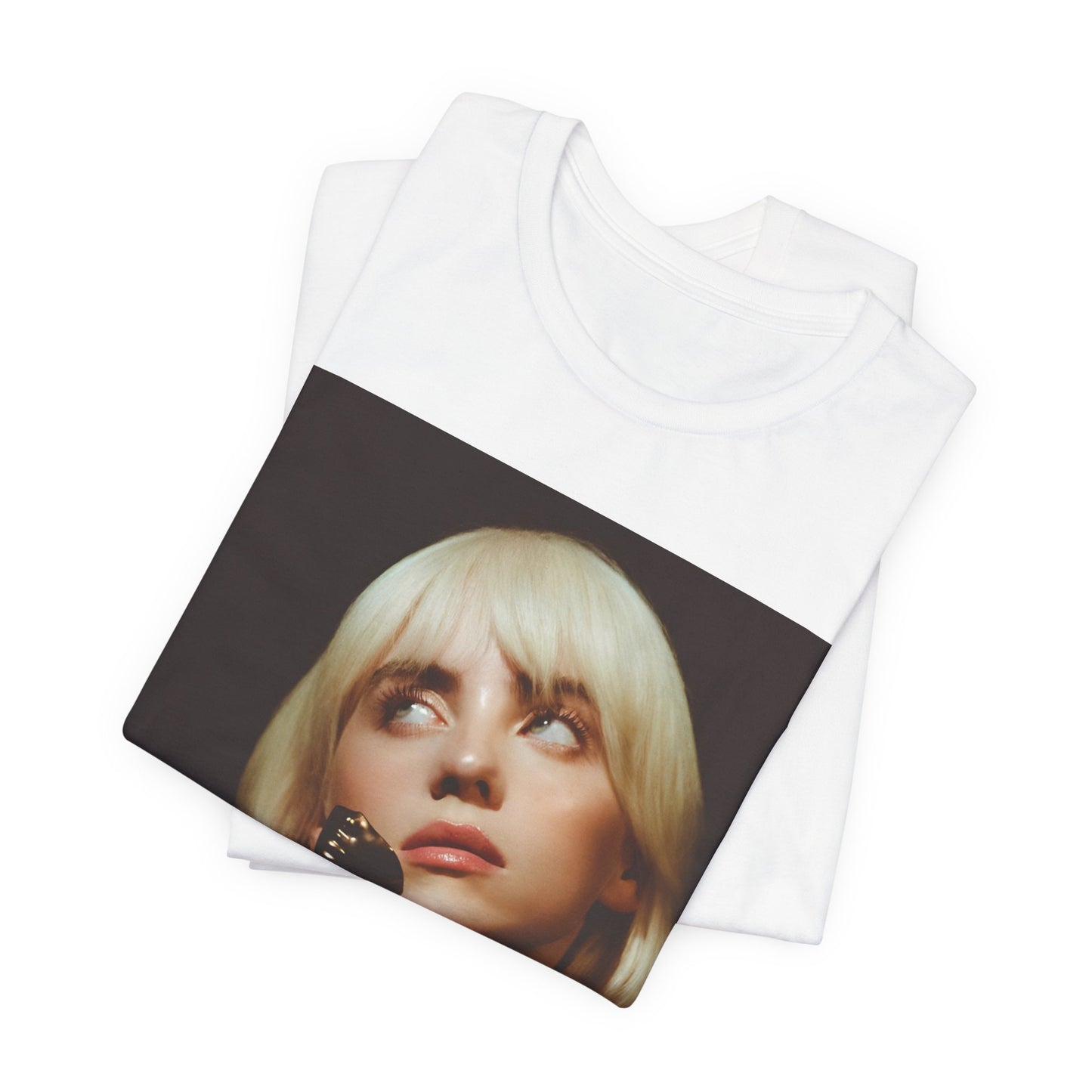 A soft, close-up portrait of Billie Eilish with dark hair looking down thoughtfully, printed on a graphic t-shirt.