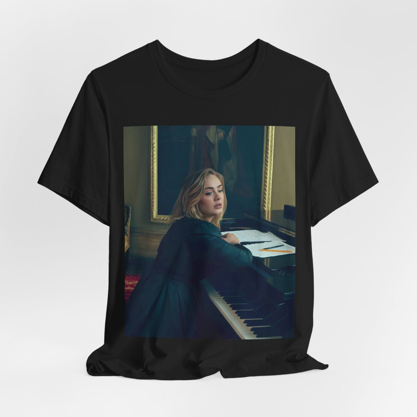 A black graphic t-shirt featuring a black and white photo of Adele sitting at a piano, with a focused and emotional expression as if performing.