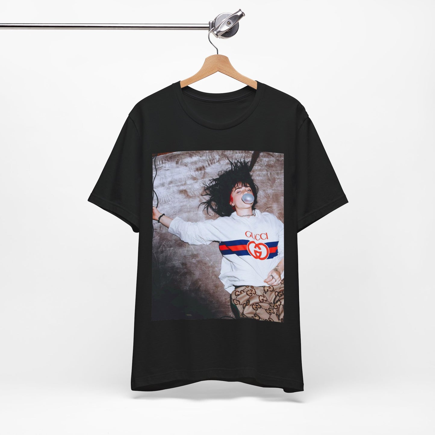 An overhead, pop-art style photo of Billie Eilish lying on the floor wearing a Gucci sweatshirt and blowing a bubblegum bubble, printed on a graphic t-shirt.