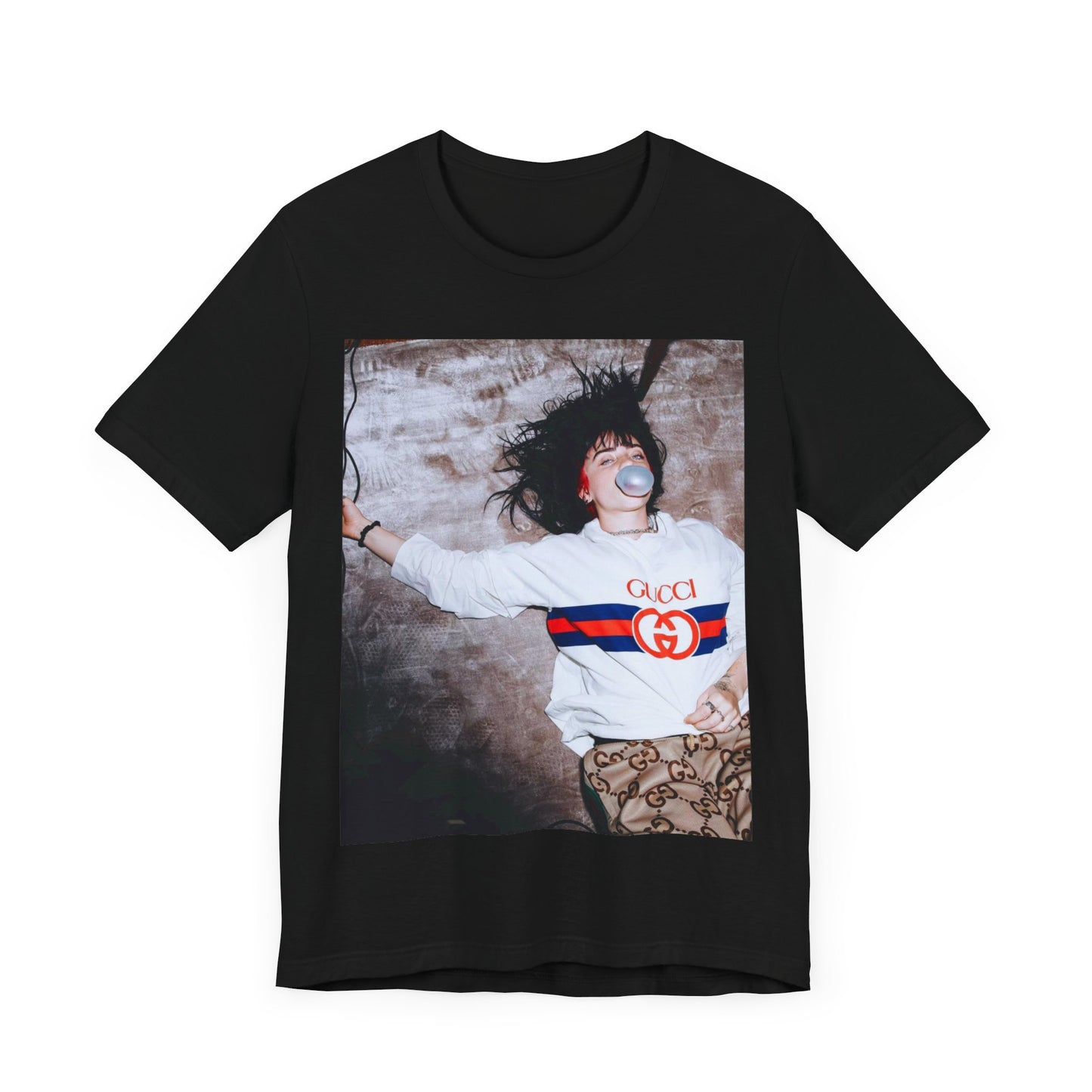 An overhead, pop-art style photo of Billie Eilish lying on the floor wearing a Gucci sweatshirt and blowing a bubblegum bubble, printed on a graphic t-shirt.