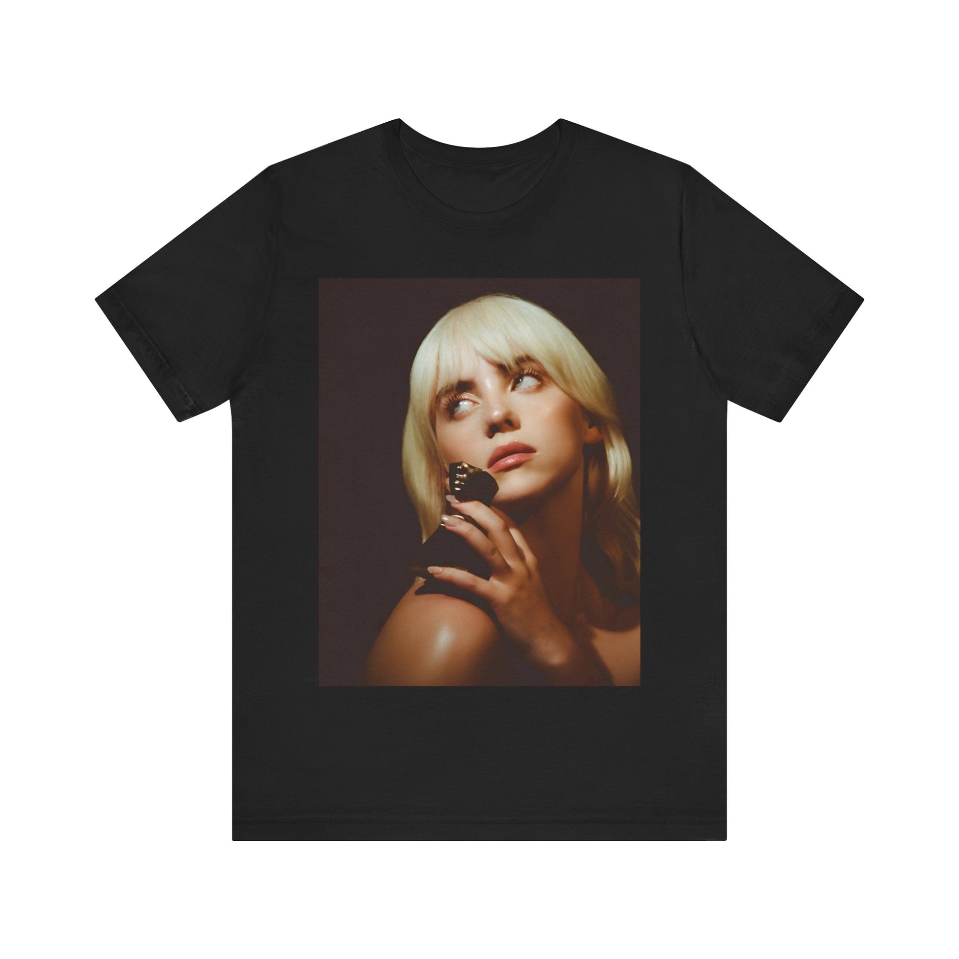 A soft, close-up portrait of Billie Eilish with dark hair looking down thoughtfully, printed on a graphic t-shirt.