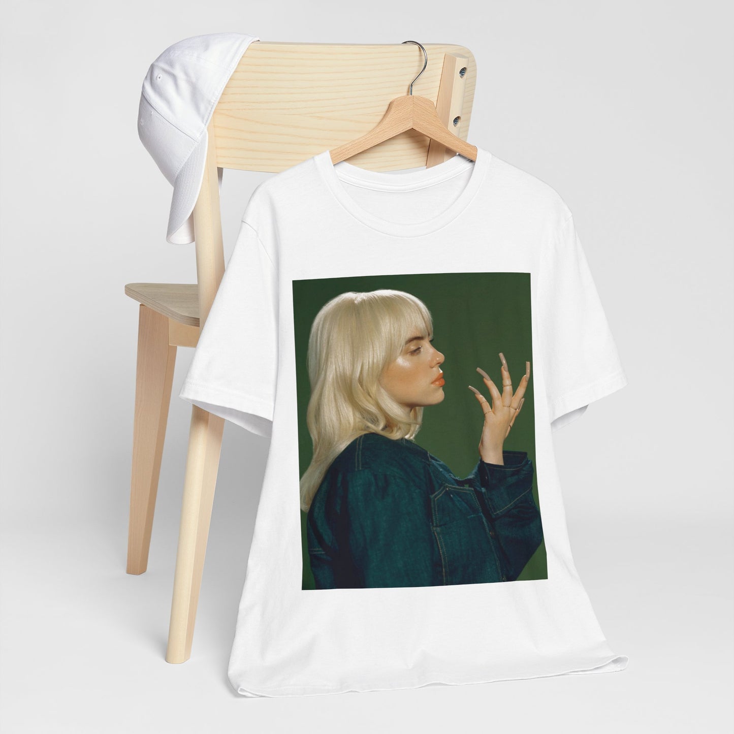 A vintage-style portrait of Billie Eilish with platinum blonde hair and long nails, wearing a denim jacket against a green background.