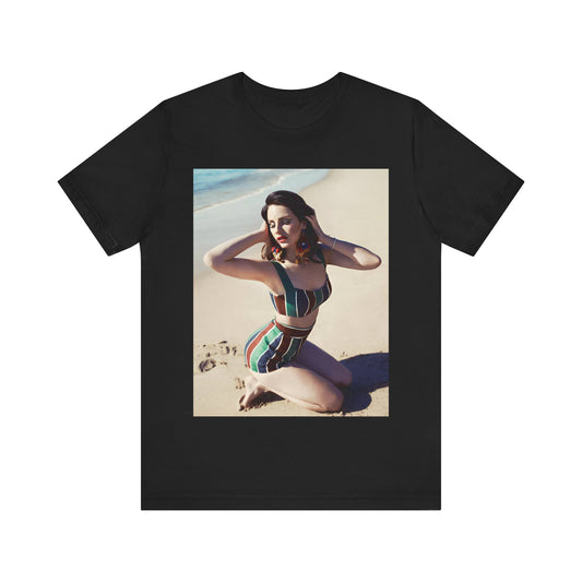 Lana Del Rey kneeling on a beach and posing in a vintage-style, high-waisted striped swimsuit, printed on a graphic t-shirt.