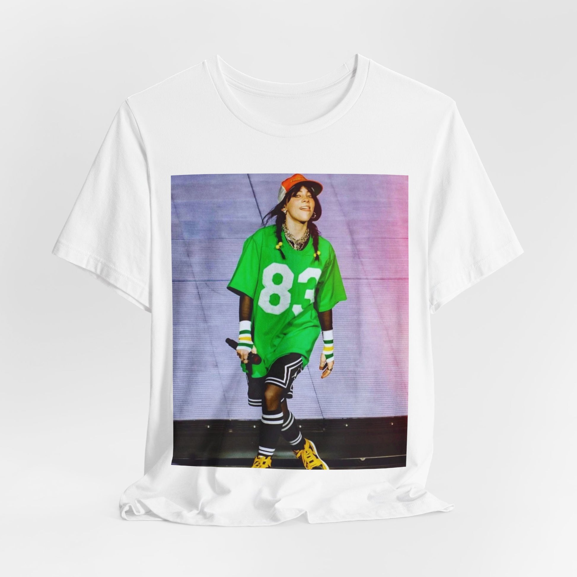 Billie Eilish performing on stage wearing a large green basketball jersey with the number 83 and an orange backwards cap.