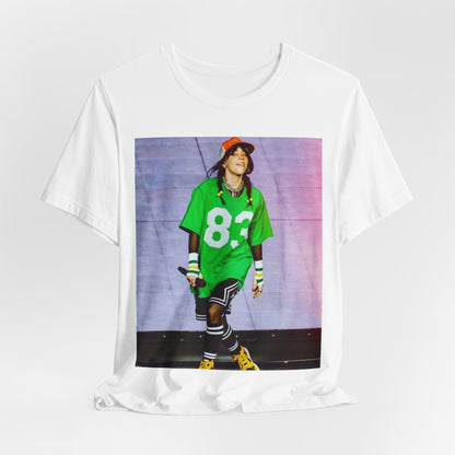 Billie Eilish performing on stage wearing a large green basketball jersey with the number 83 and an orange backwards cap.