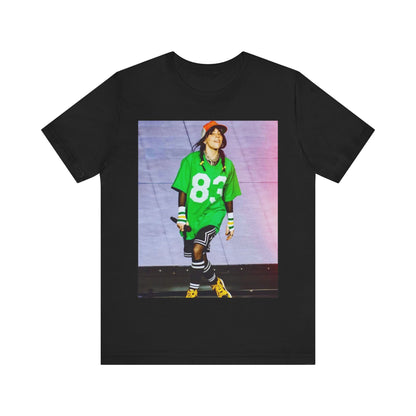 Billie Eilish performing on stage wearing a large green basketball jersey with the number 83 and an orange backwards cap.