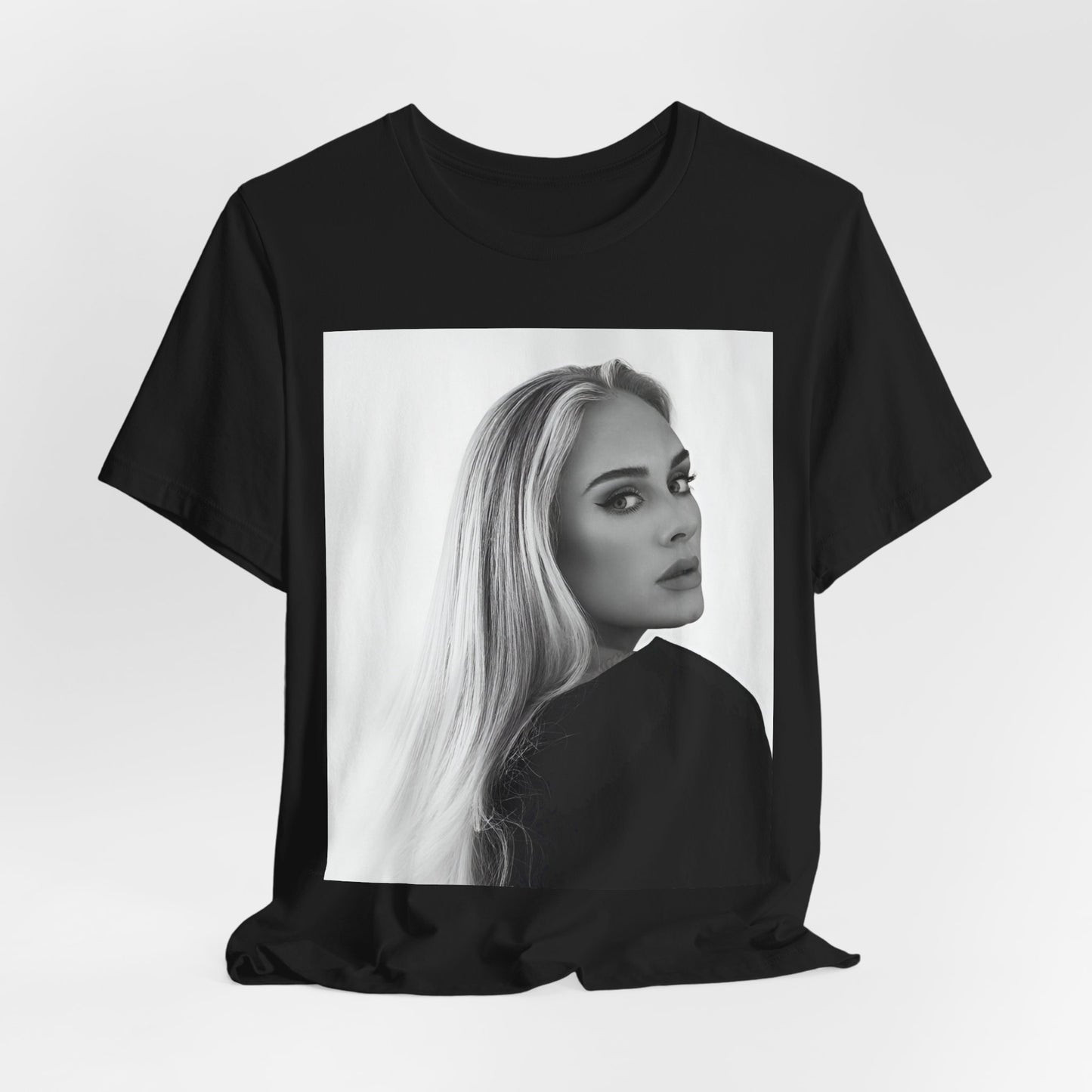 A black graphic t-shirt featuring a black and white, monochromatic portrait of Adele, showing her with a serene or thoughtful expression.
