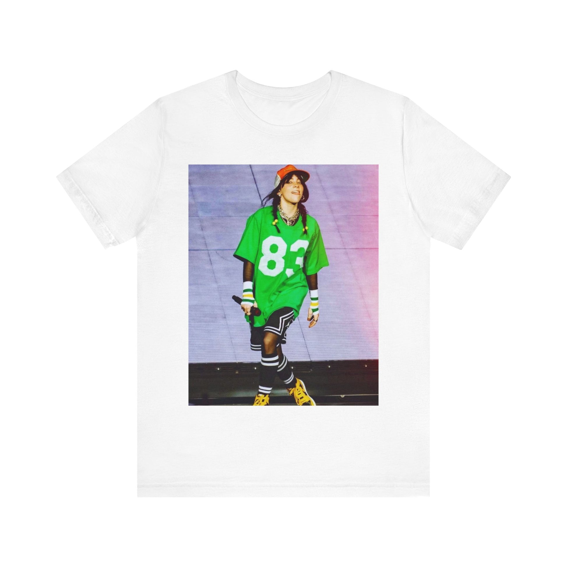 Billie Eilish performing on stage wearing a large green basketball jersey with the number 83 and an orange backwards cap.