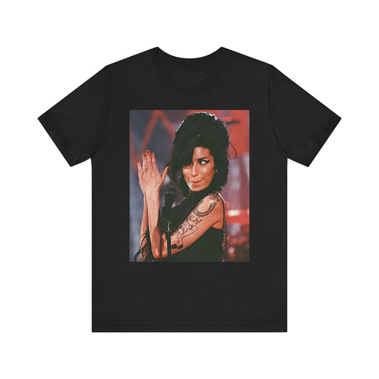 A black graphic t-shirt featuring a photo of Amy Winehouse performing live on stage in 2008, with her signature beehive and expressive singing.