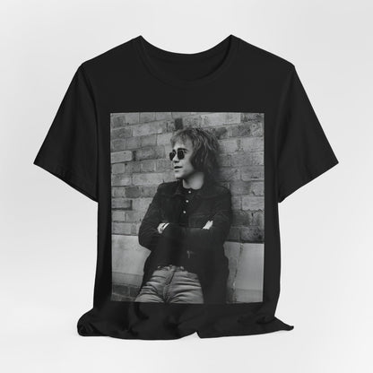 A black graphic t-shirt featuring a vintage graphic related to Elton John's 'Farewell Yellow Brick Road' tour.