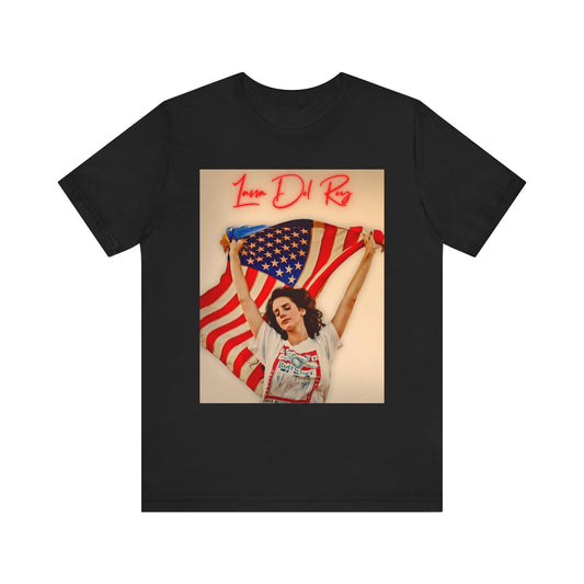 Lana Del Rey holding a large American flag behind her, with her name in red neon script, printed on a graphic t-shirt