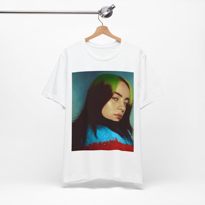 A close-up portrait of Billie Eilish with her signature green-root and black hair, wearing a blue and red sweater, printed on a graphic t-shirt.
