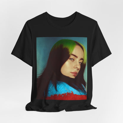 A close-up portrait of Billie Eilish with her signature green-root and black hair, wearing a blue and red sweater, printed on a graphic t-shirt.