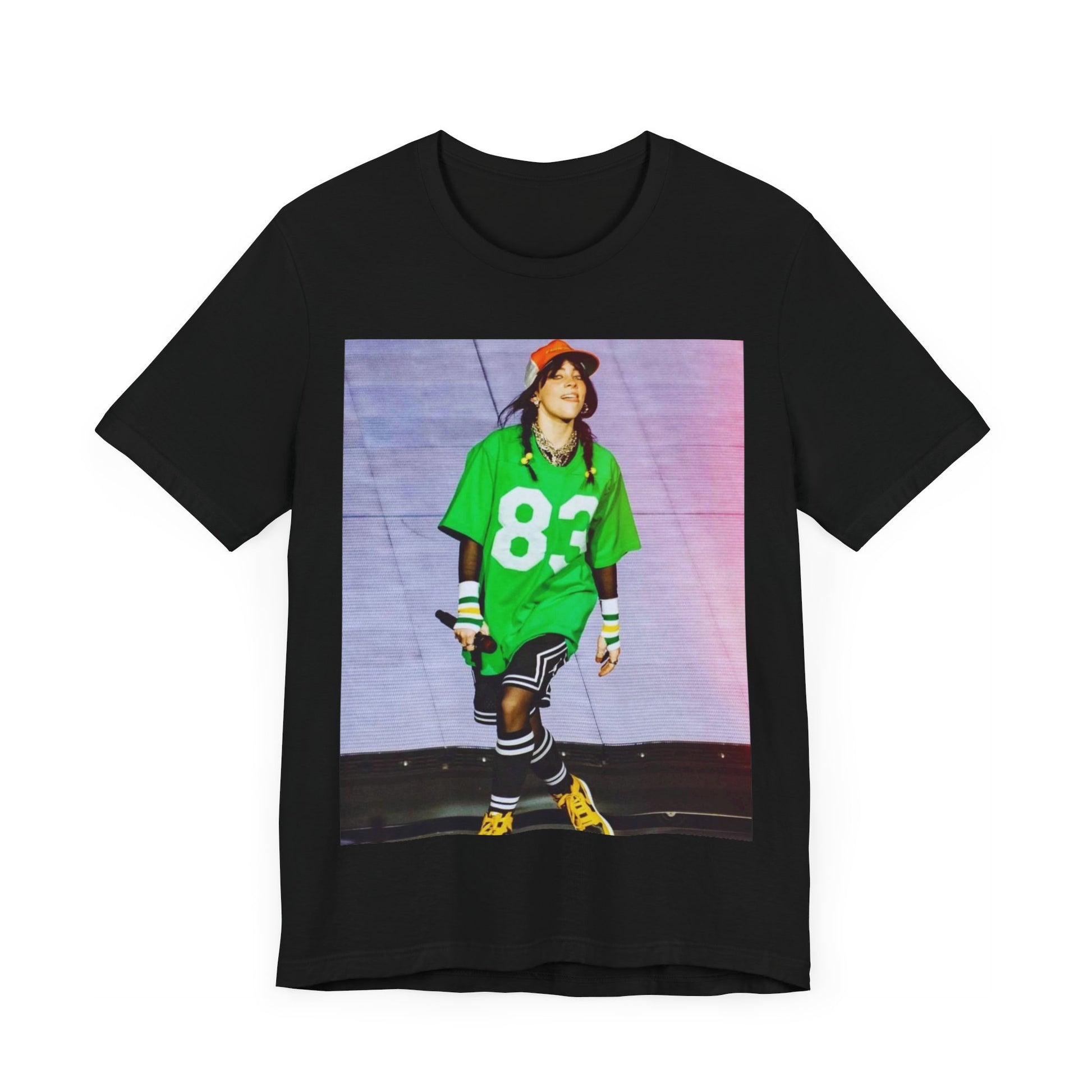 Billie Eilish performing on stage wearing a large green basketball jersey with the number 83 and an orange backwards cap.