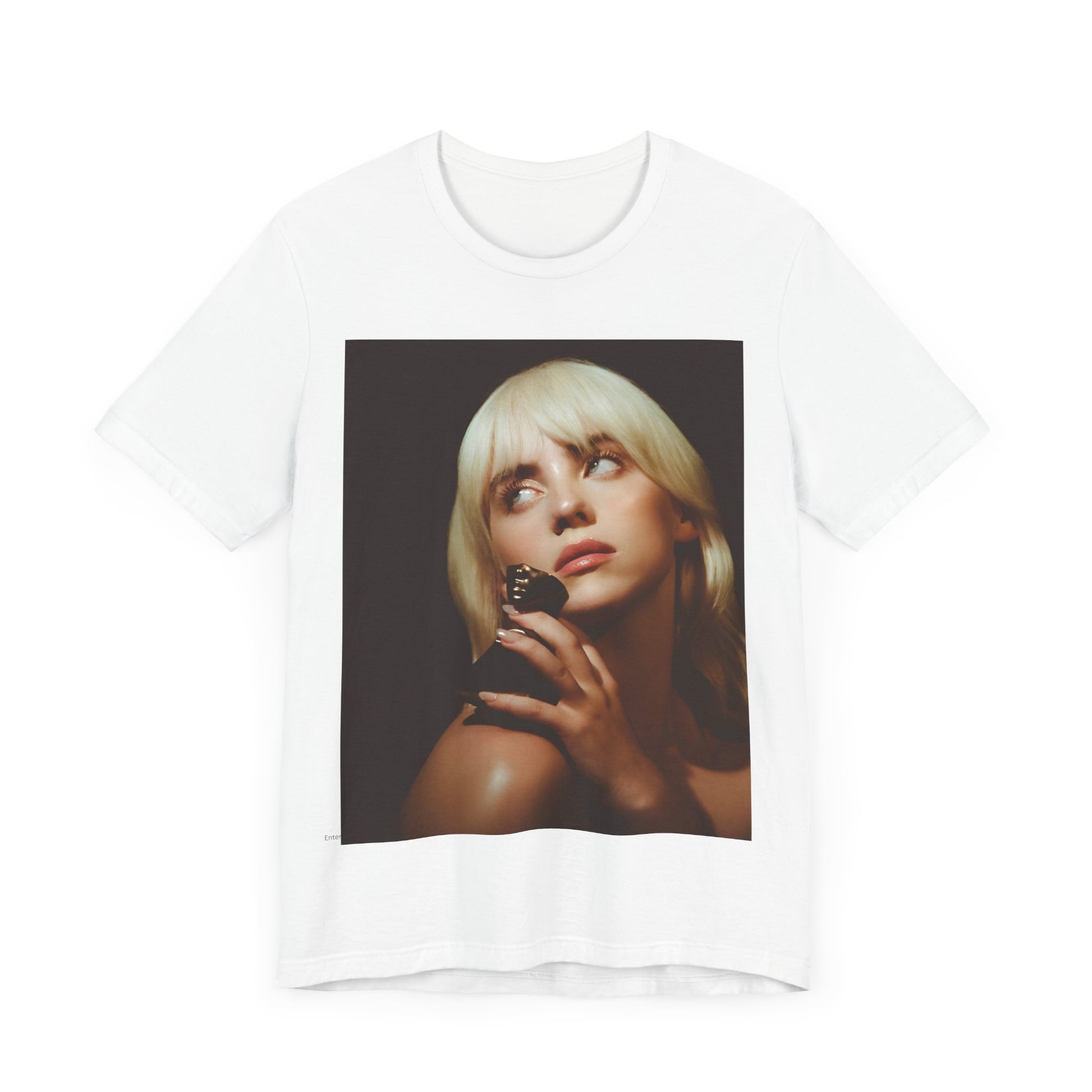 A soft, close-up portrait of Billie Eilish with dark hair looking down thoughtfully, printed on a graphic t-shirt.