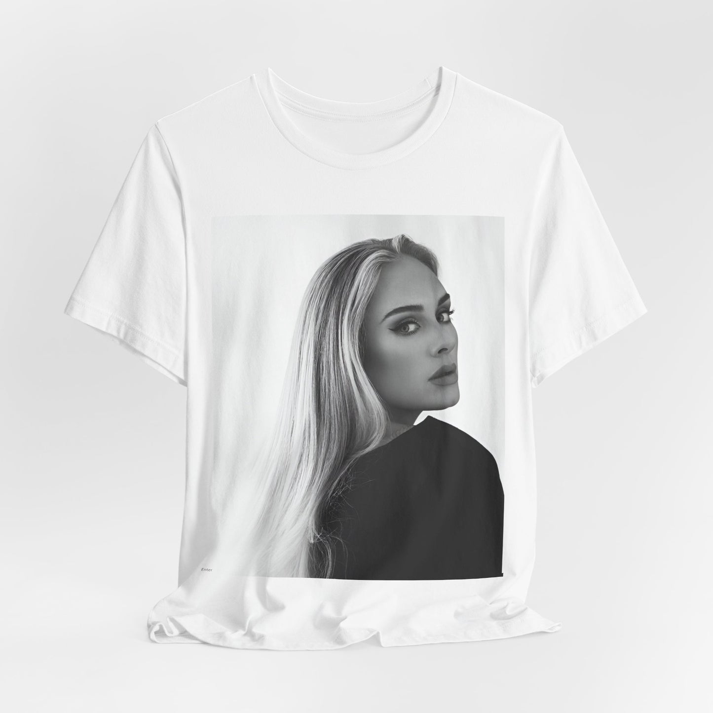 A black graphic t-shirt featuring a black and white, monochromatic portrait of Adele, showing her with a serene or thoughtful expression.