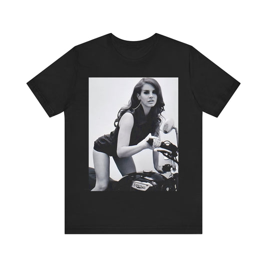 Black and white photo of Lana Del Rey posing on a vintage Triumph motorcycle, printed on a graphic t-shirt.