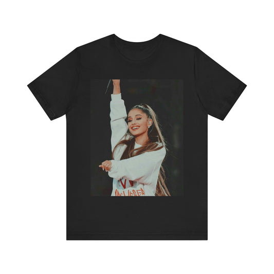 A black graphic t-shirt featuring a dynamic graphic or photo of Ariana Grande performing live on stage.
