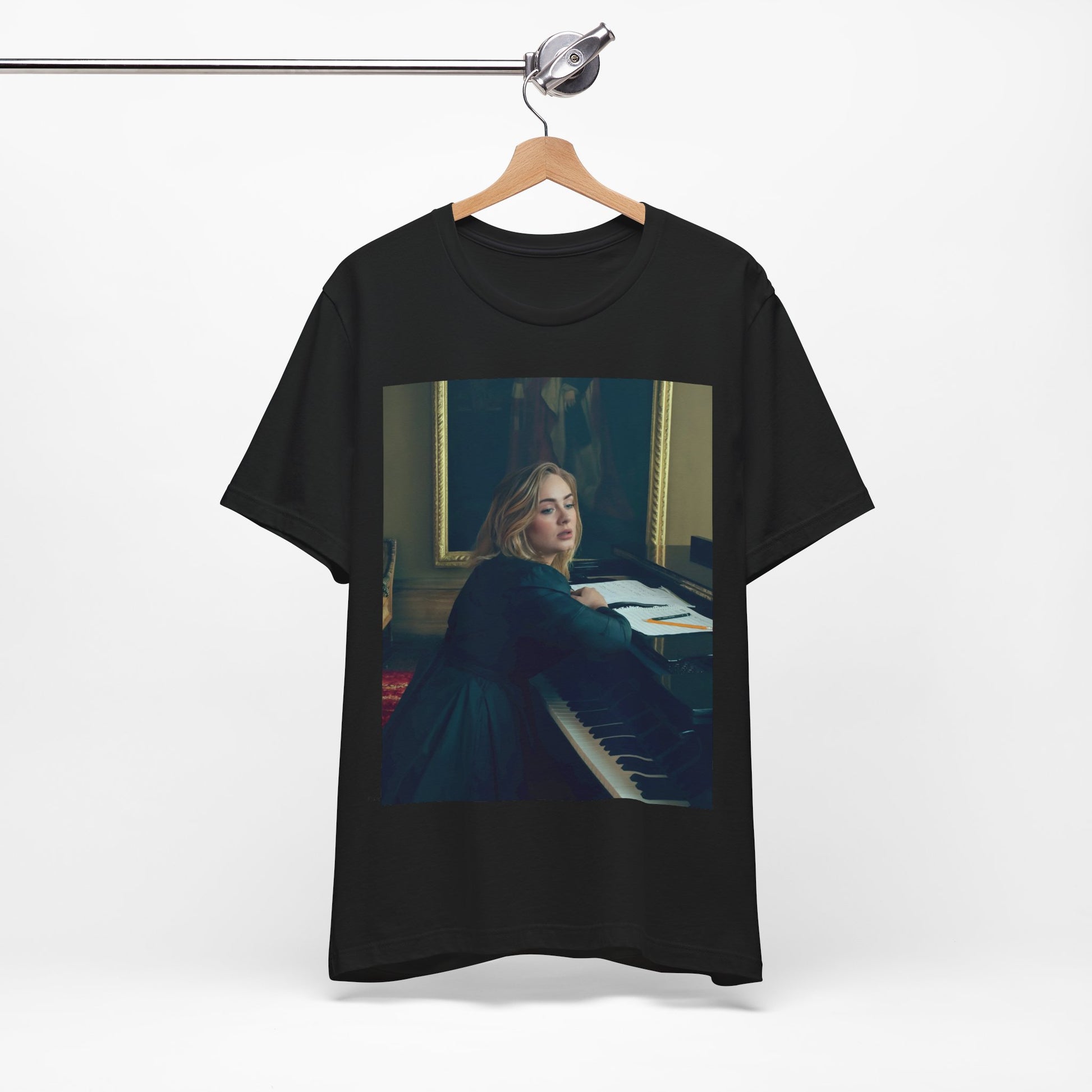 A black graphic t-shirt featuring a black and white photo of Adele sitting at a piano, with a focused and emotional expression as if performing.