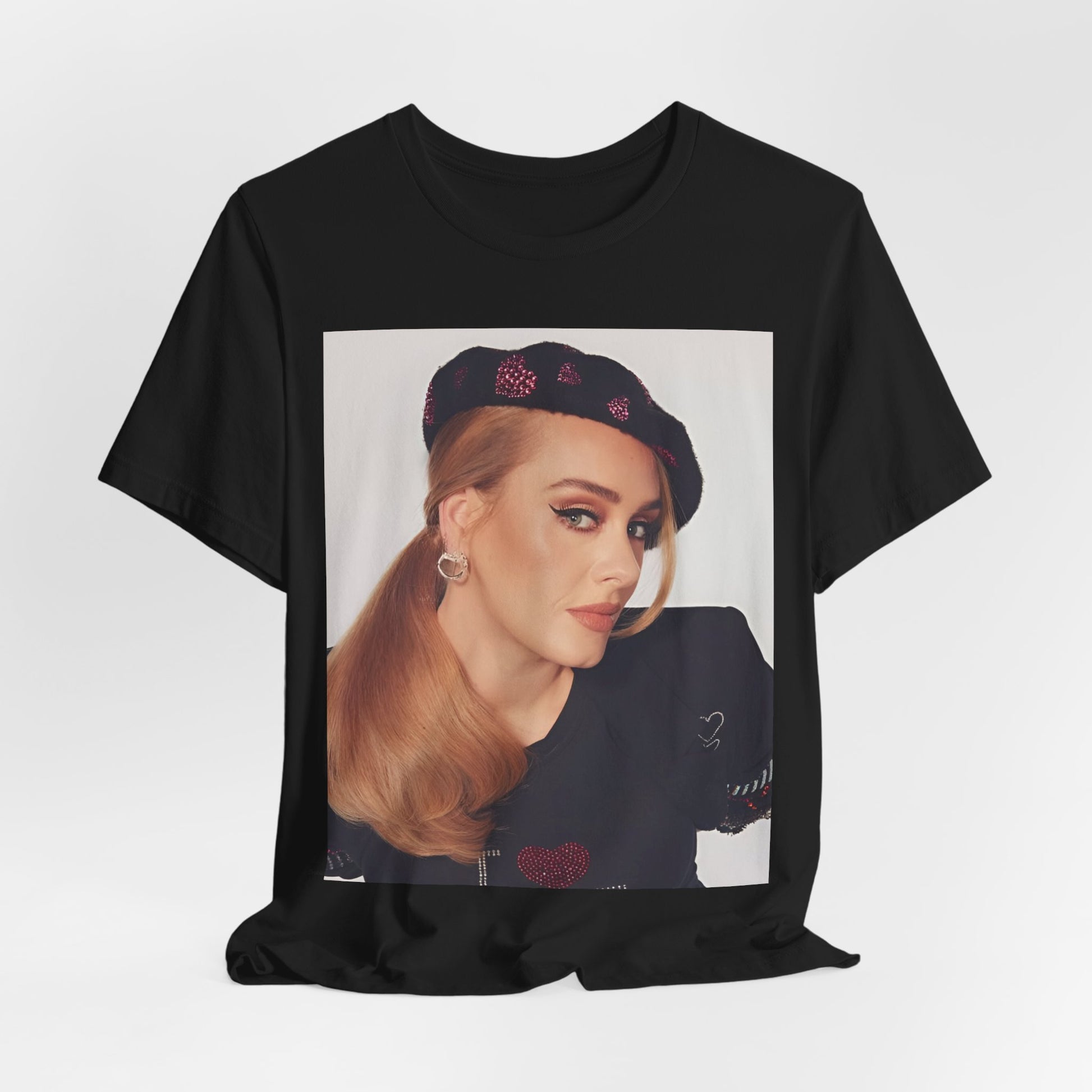 A black graphic t-shirt featuring a black and white photo of Adele wearing a heart-shaped beret, with a gentle or smiling expression.