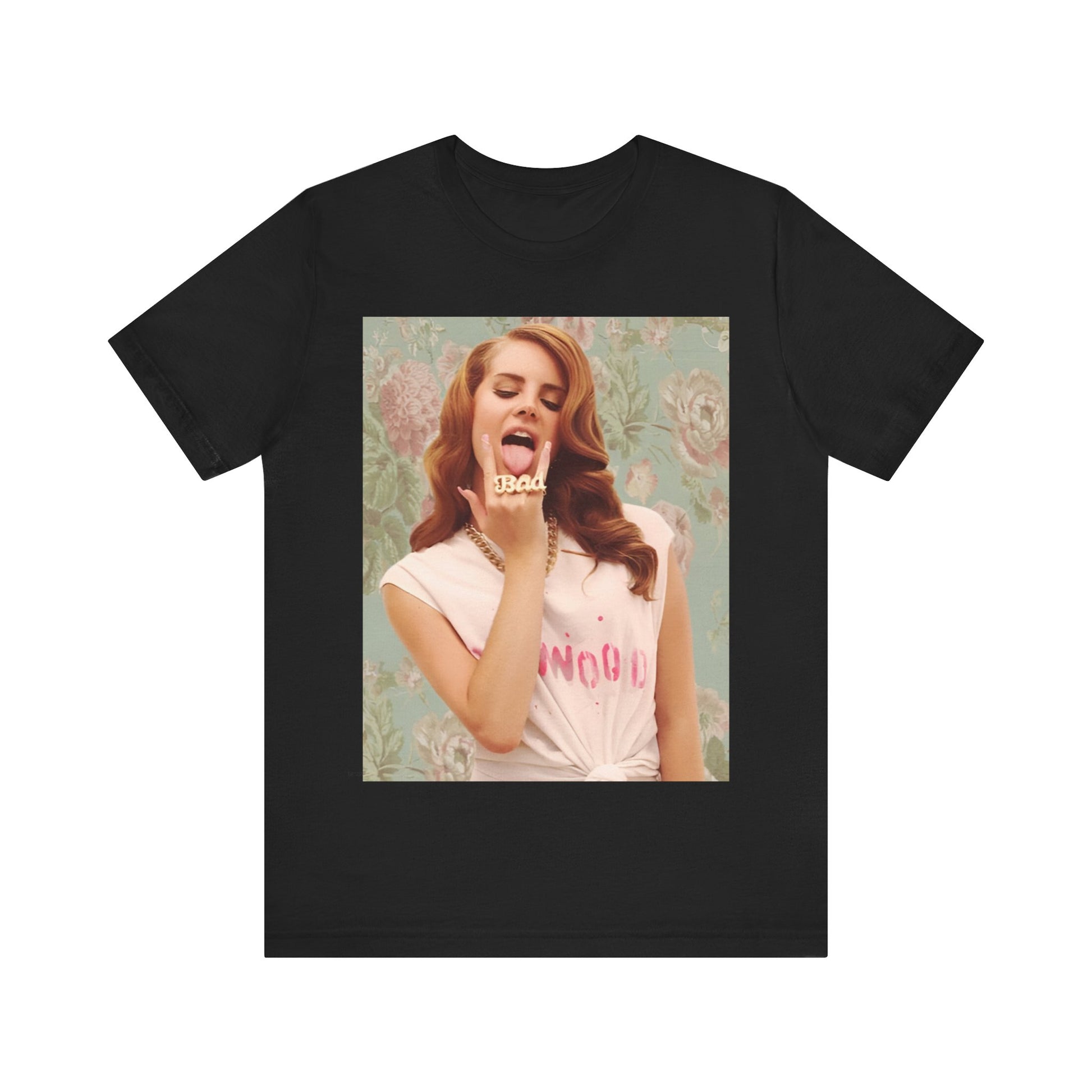 Lana Del Rey sticking her tongue out and wearing a "BAD" ring, posing against floral wallpaper, printed on a graphic tee.