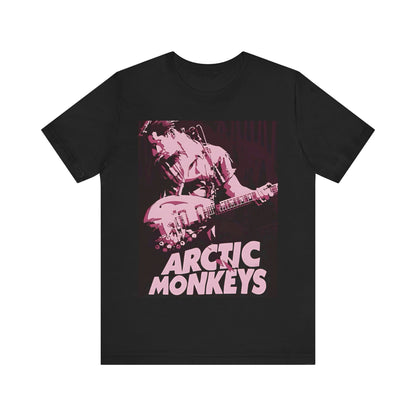 A black graphic t-shirt featuring the Arctic Monkeys logo in a prominent pink color, creating an aesthetic look.