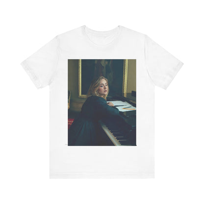 A black graphic t-shirt featuring a black and white photo of Adele sitting at a piano, with a focused and emotional expression as if performing.
