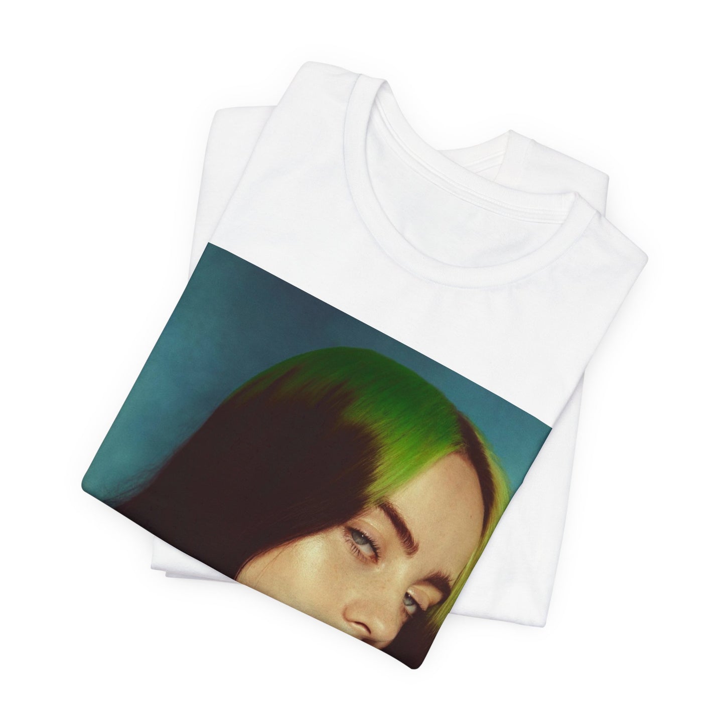 A close-up portrait of Billie Eilish with her signature green-root and black hair, wearing a blue and red sweater, printed on a graphic t-shirt.
