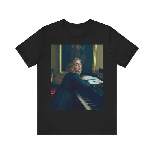 A black graphic t-shirt featuring a black and white photo of Adele sitting at a piano, with a focused and emotional expression as if performing.